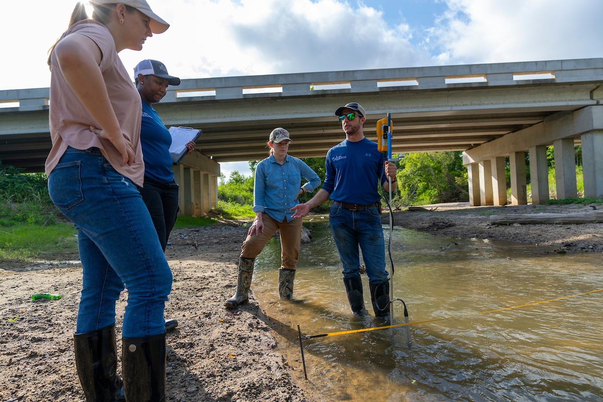 People standing in a creek with instruments to measure water quality